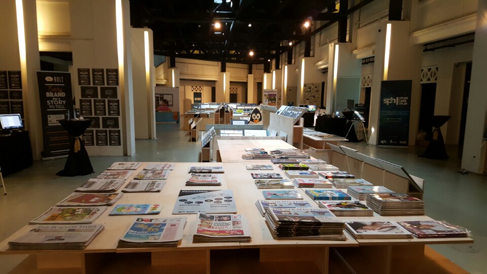 Magazines and newspapers lay on light brown wooden tables inside a museum