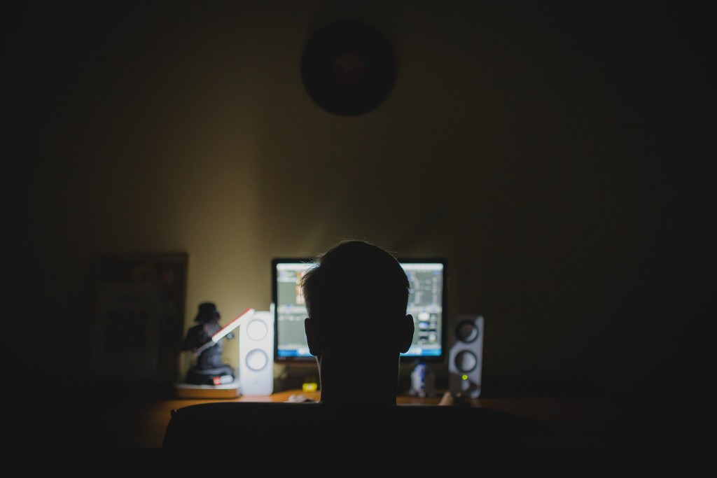 dark room with man sitting in char typing on computer